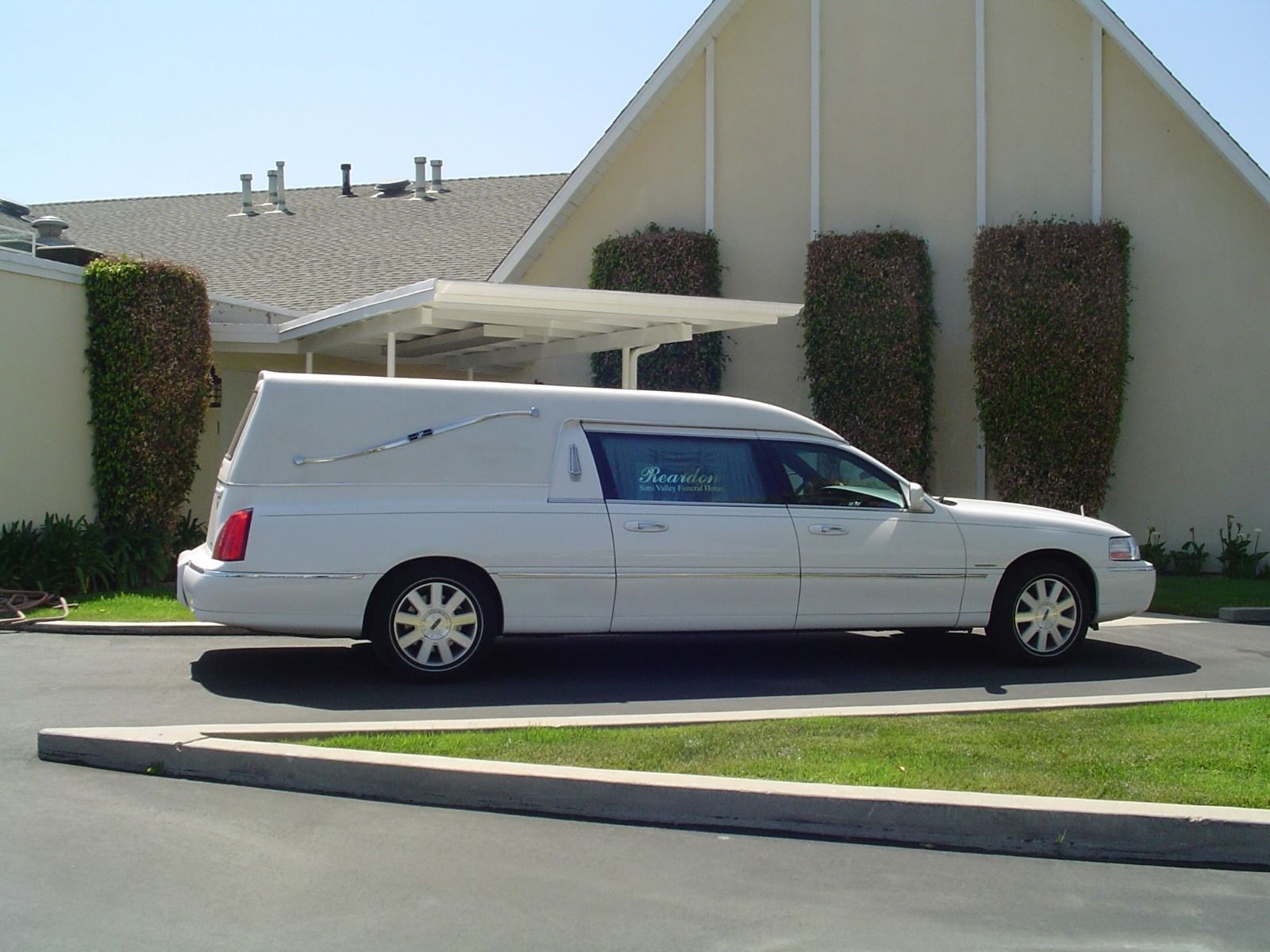 White hearse parked outside a light-colored funeral home.