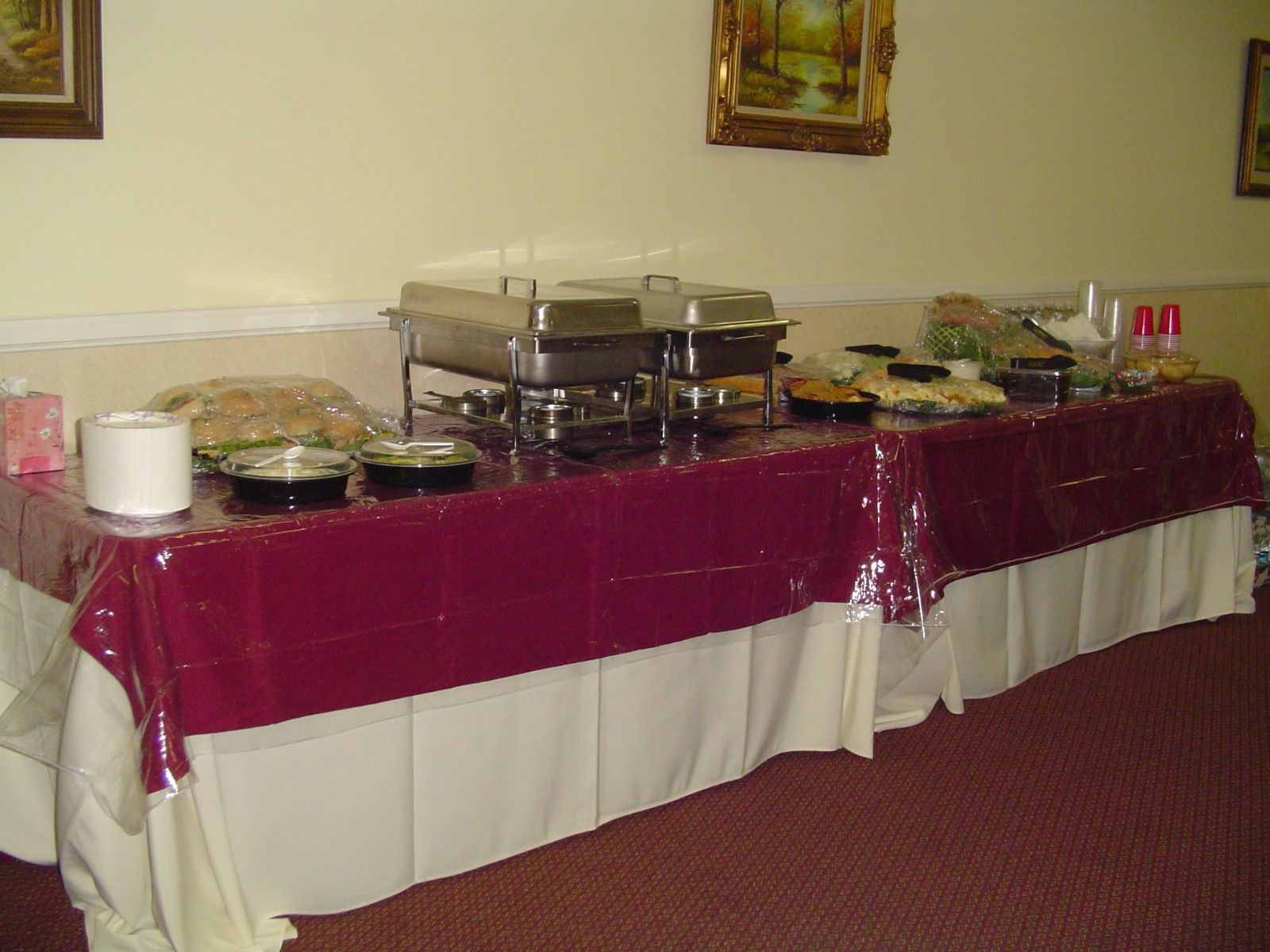 Buffet table with various food dishes and chafing dishes, covered in burgundy and white tablecloths.