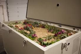 A large, white rectangular composting container with colorful flowers and straw inside, lid open.