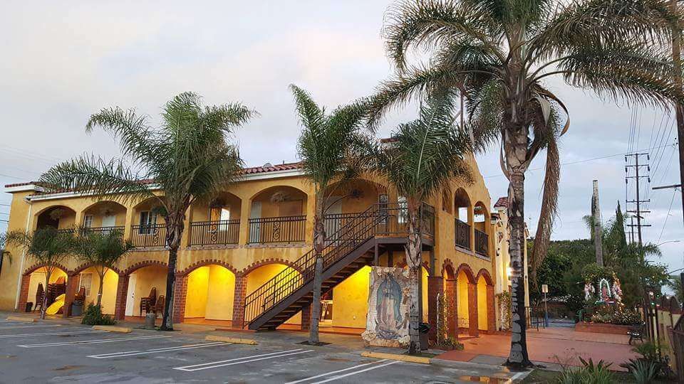 Two-story yellow stucco building with arched windows, palm trees, and an exterior staircase.