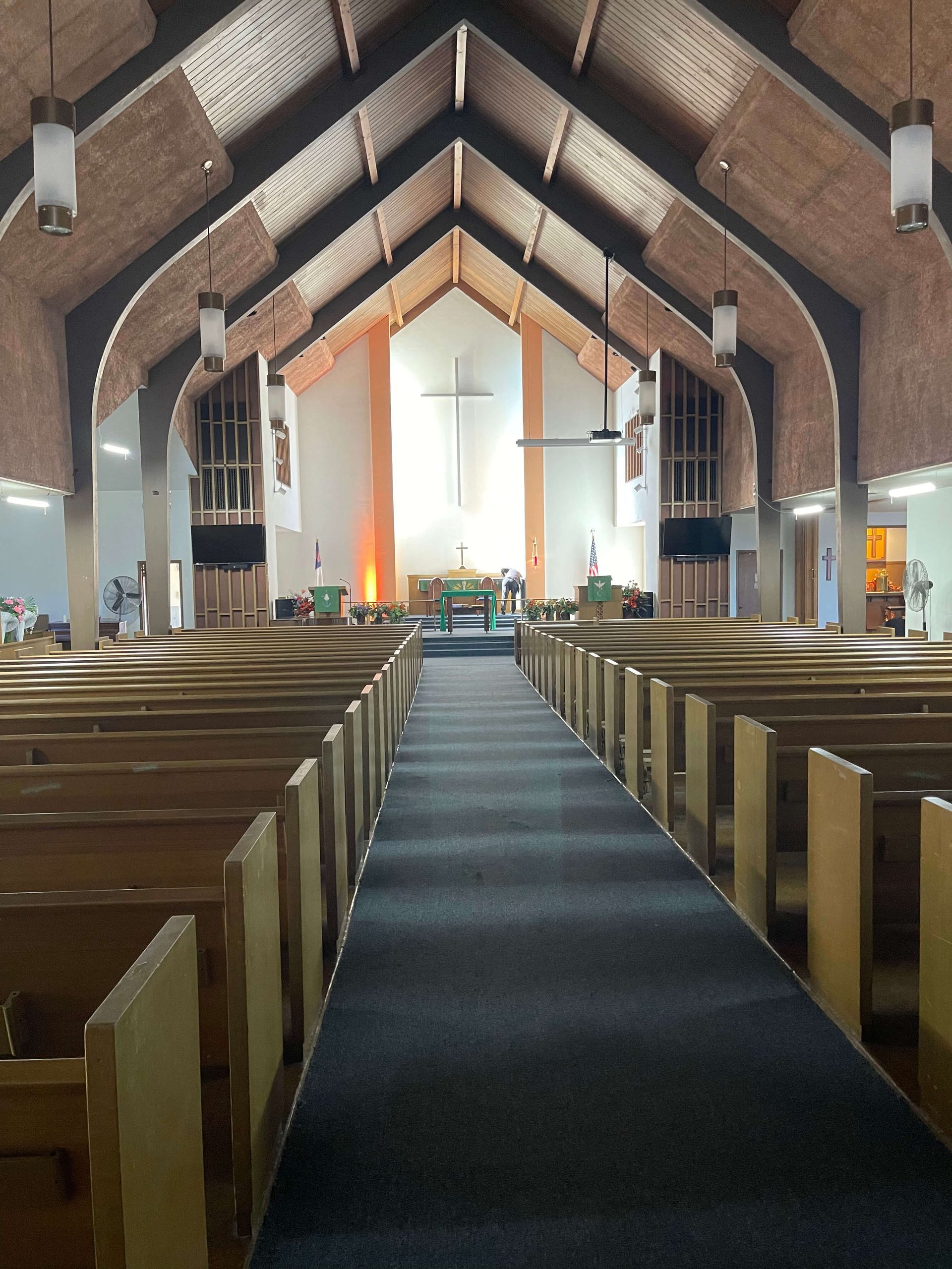 Interior view of a church with rows of wooden pews leading to an altar with a large cross.