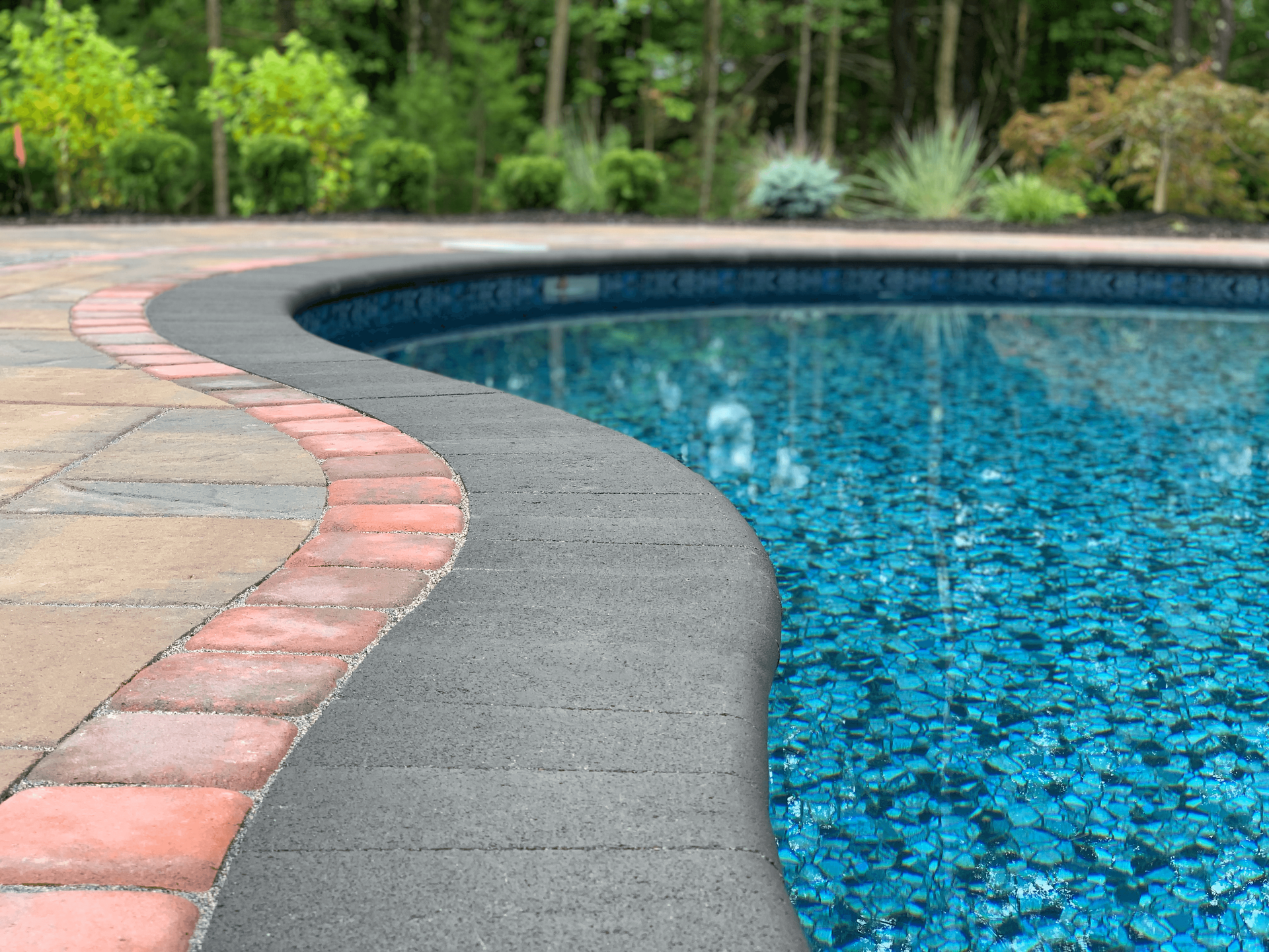A swimming pool with a brick border and trees in the background.