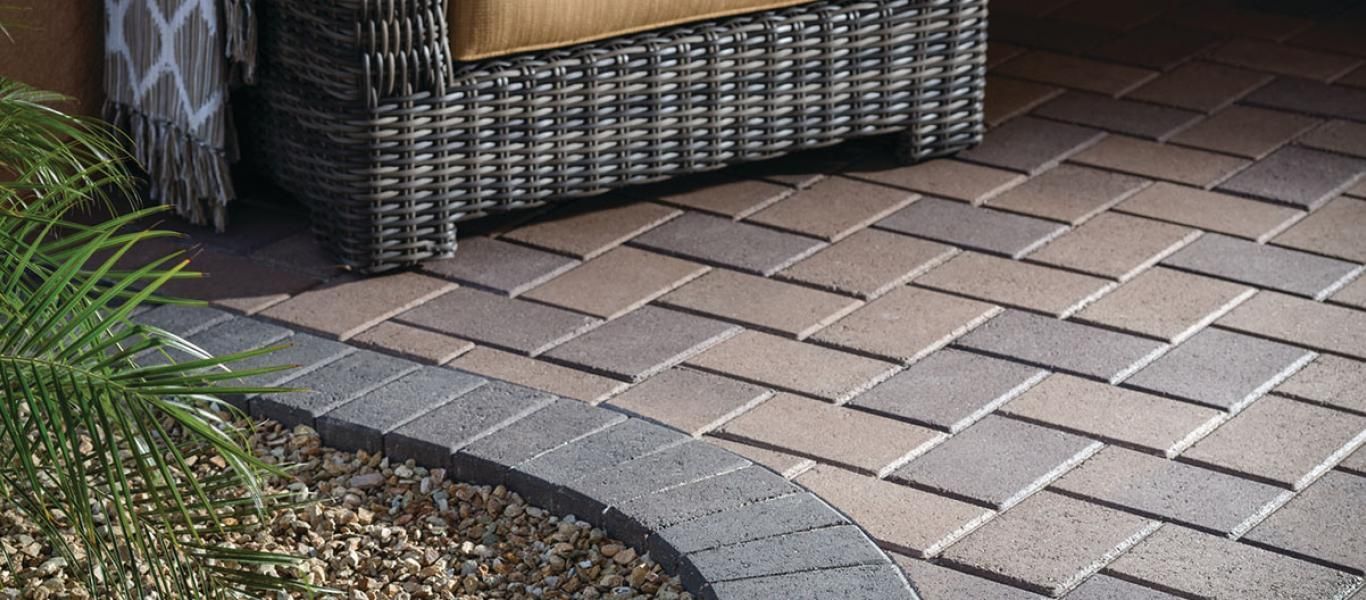 A chair is sitting on a brick patio next to a wicker chair.