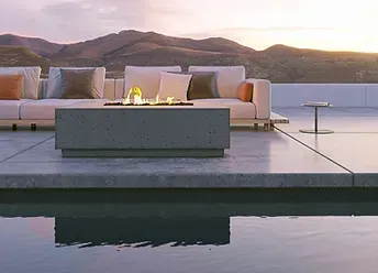 A patio with a couch and a fire pit next to a pool.