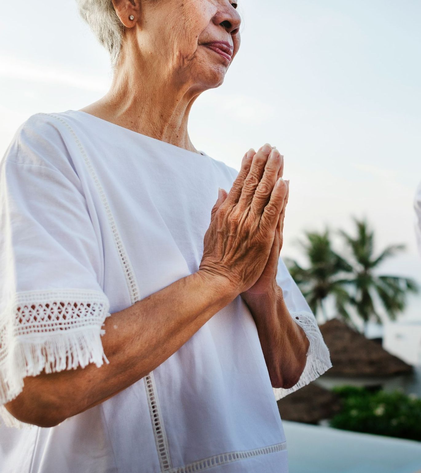 A woman in a white shirt is praying with her hands folded