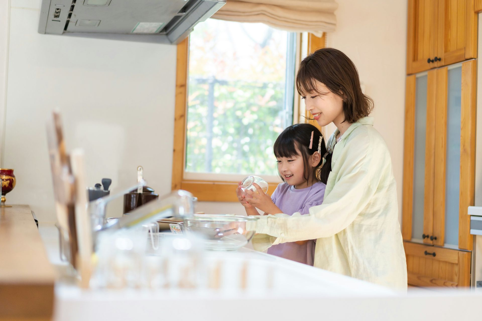 A woman and a little girl are washing dishes in a kitchen.