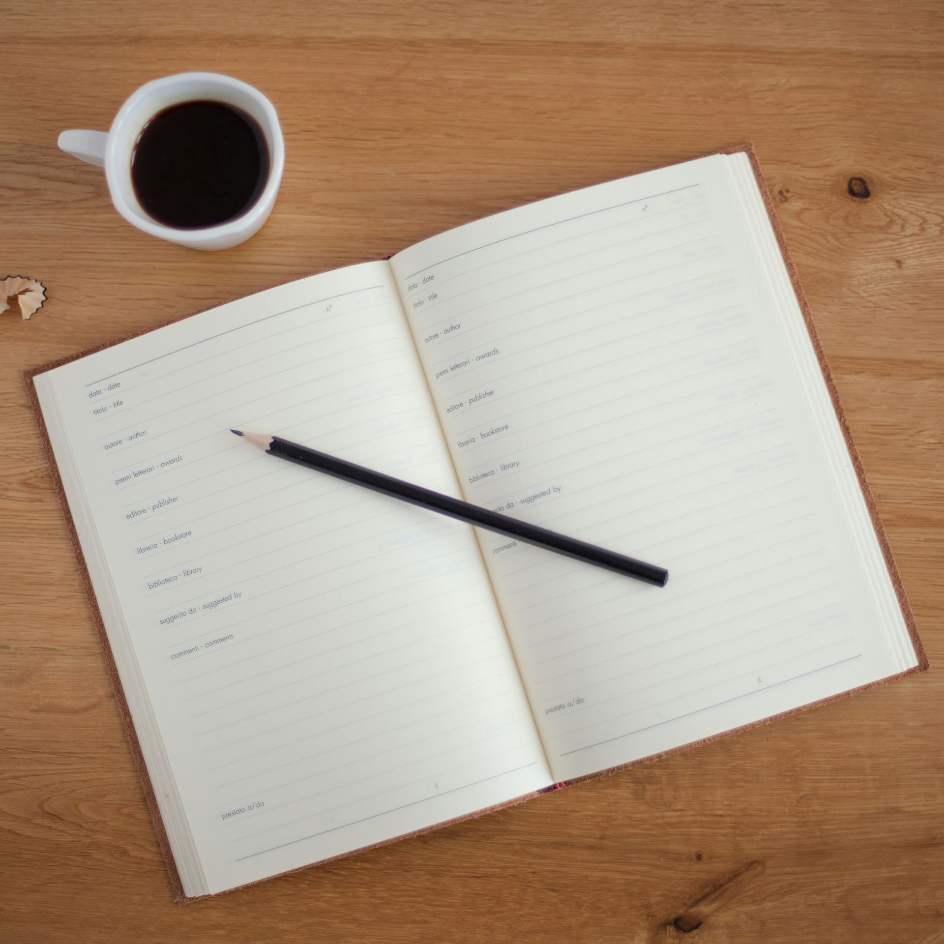 An open notebook with a pencil and a cup of coffee on a wooden table
