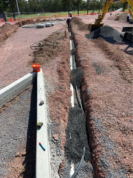 A worker in orange gloves uses a drill to connect a drain to a corrugated pipe in a trench.Orange NSW