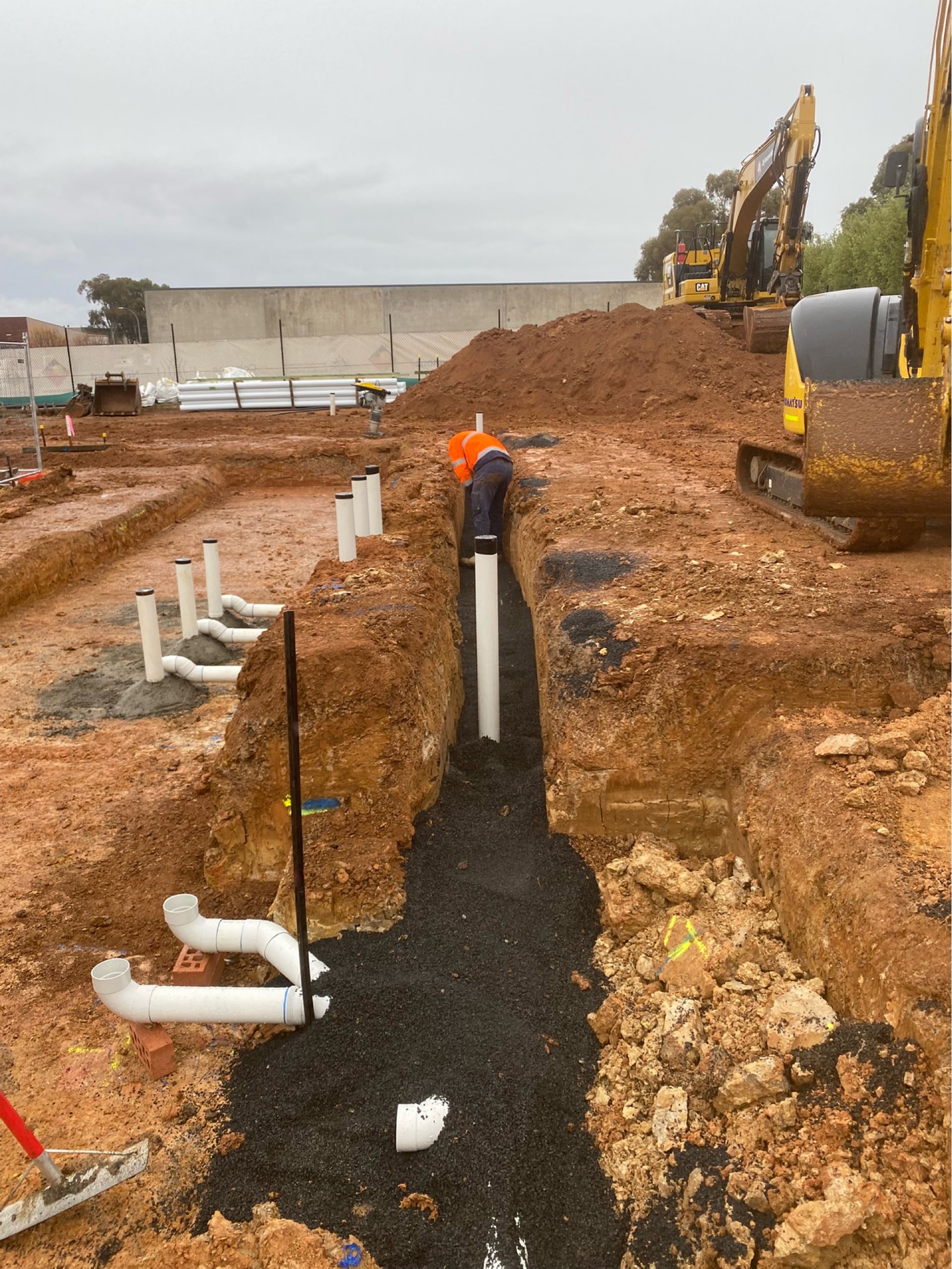Worker in safety vest installs cable near vehicles and bushes. Orange NSW