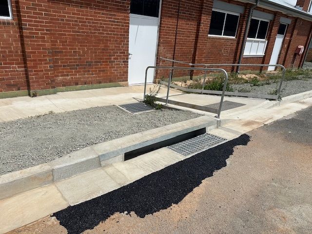 Hands in orange and black gloves tightening a clamp on white pipes with a wrench.Orange NSW