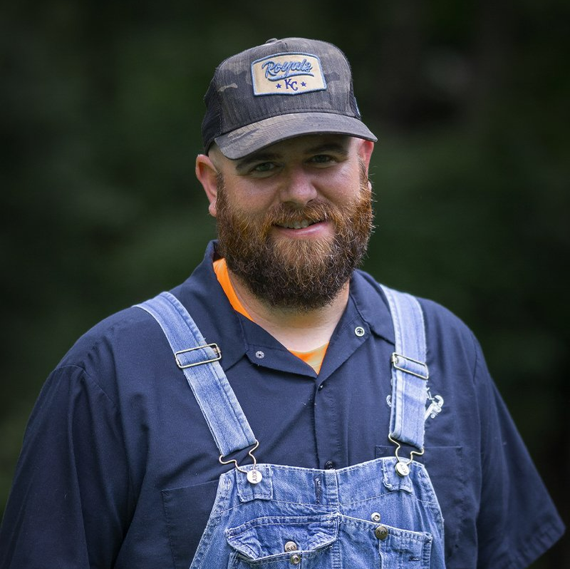 A man with a beard wearing overalls and a baseball cap