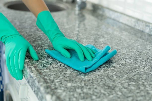 Person in green gloves cleaning a granite countertop with a blue cloth.