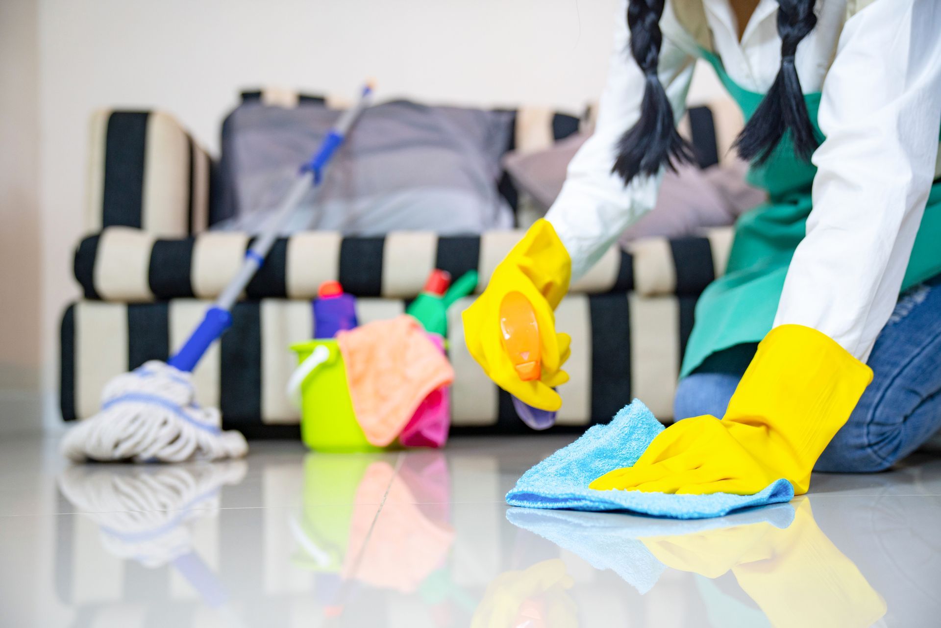 Person wearing yellow gloves cleans a floor with a blue cloth in a living room.