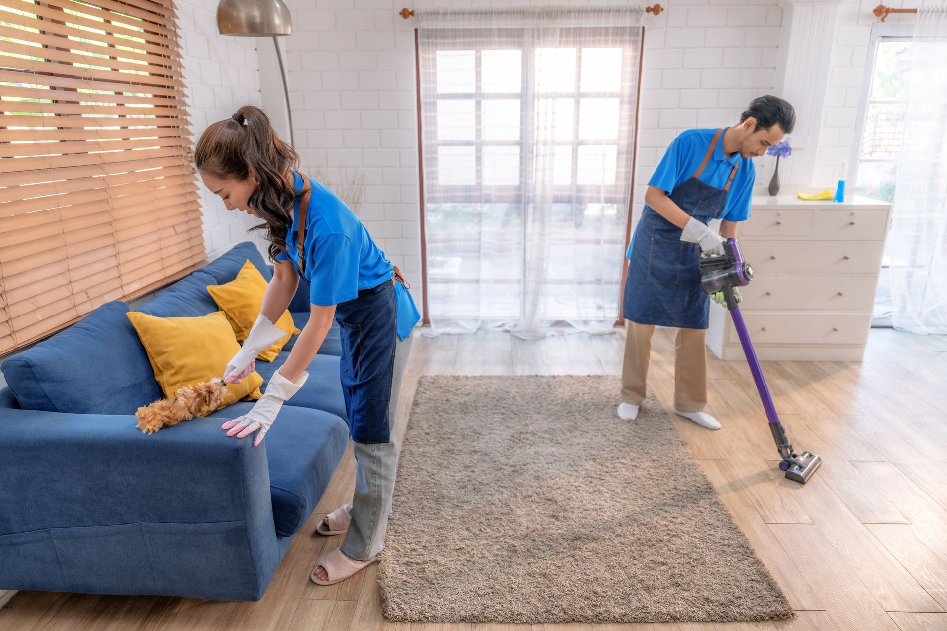 Two people cleaning carpet in an office space. One kneels giving a thumbs up, the other operates a floor cleaning machine, both smiling.
