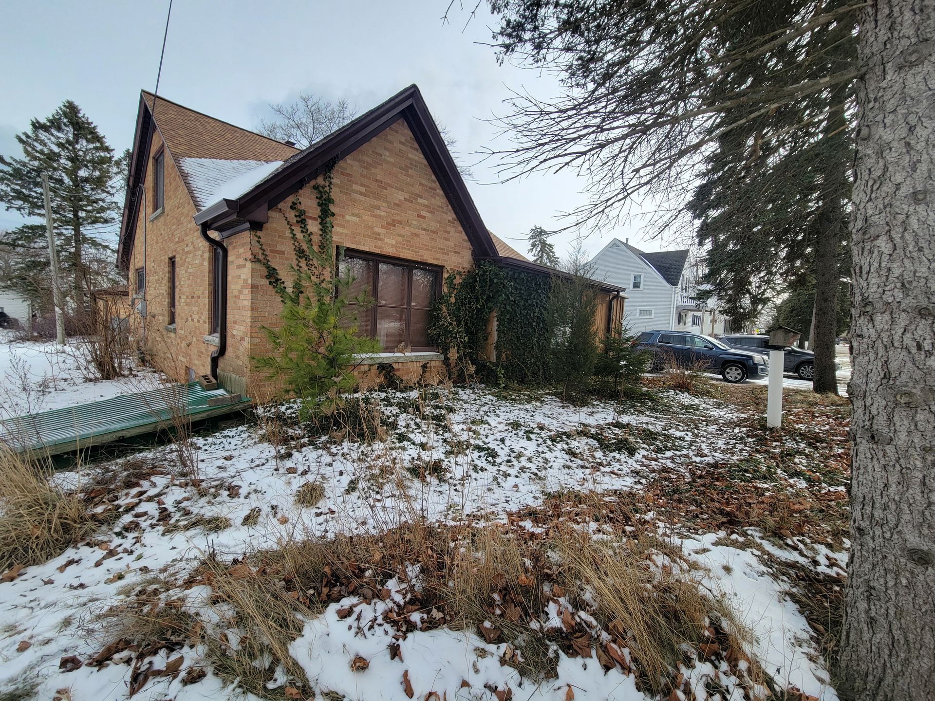 A brick house is surrounded by snow and trees.