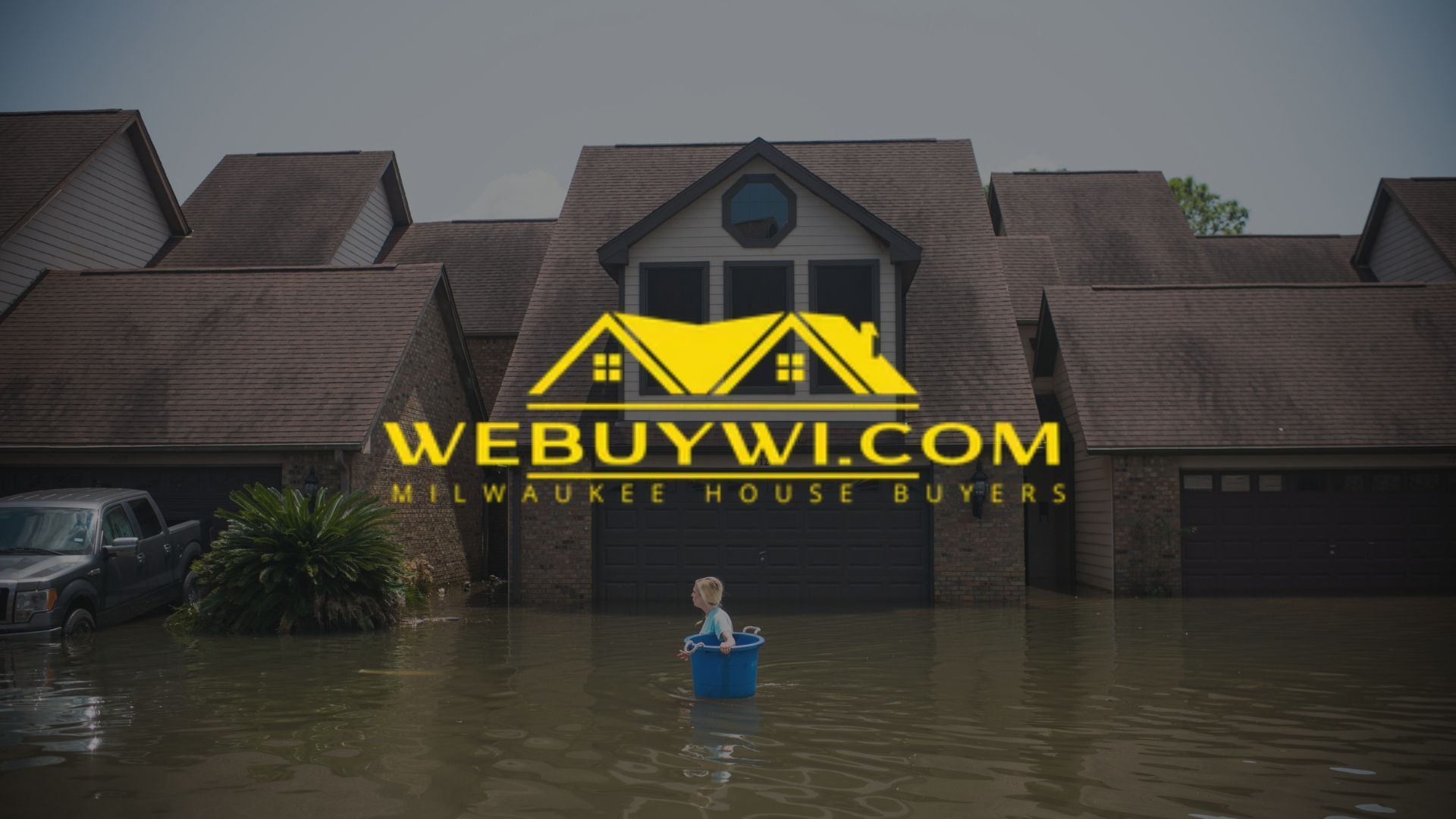 Child in a blue tub in floodwater in front of a house. 