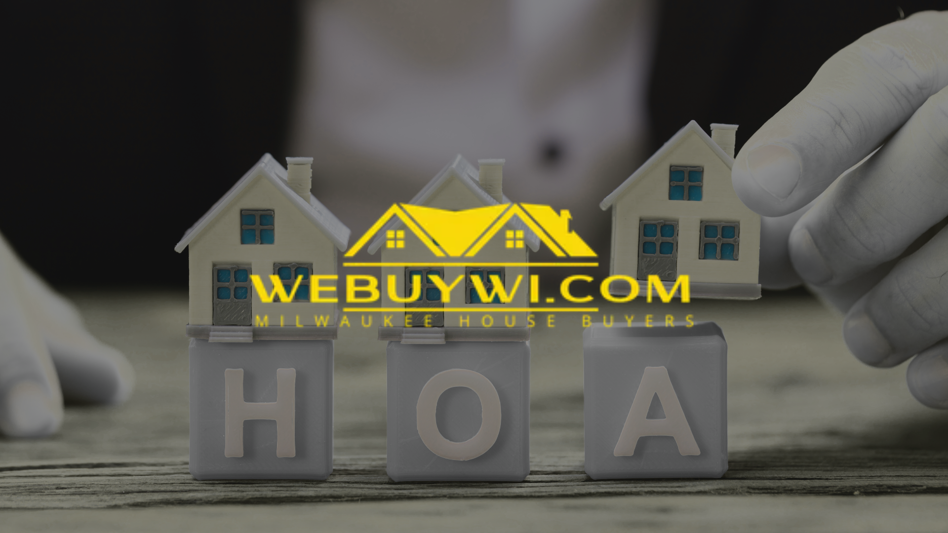 Hands holding toy houses above blocks spelling HOA, with 