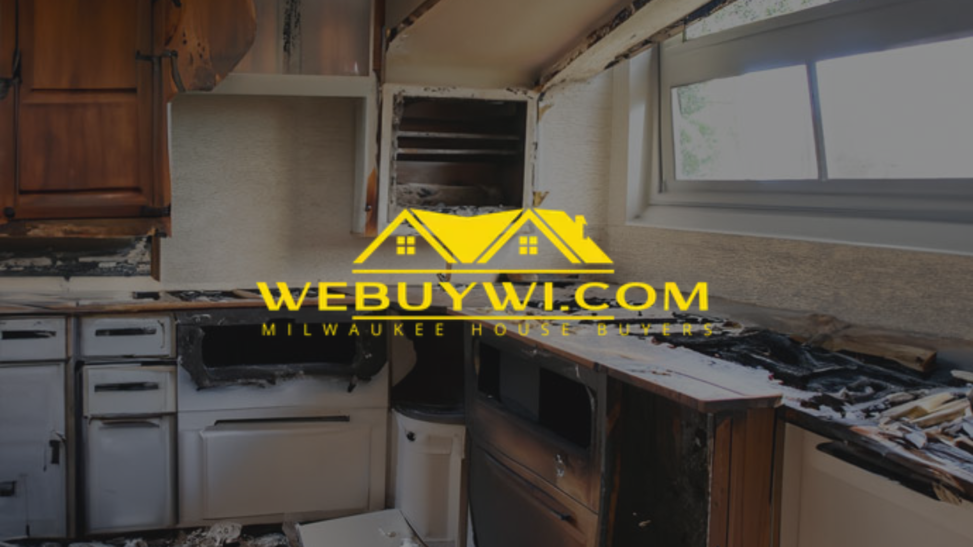 Burnt kitchen interior with damaged cabinets, appliances, and walls, likely from a fire.