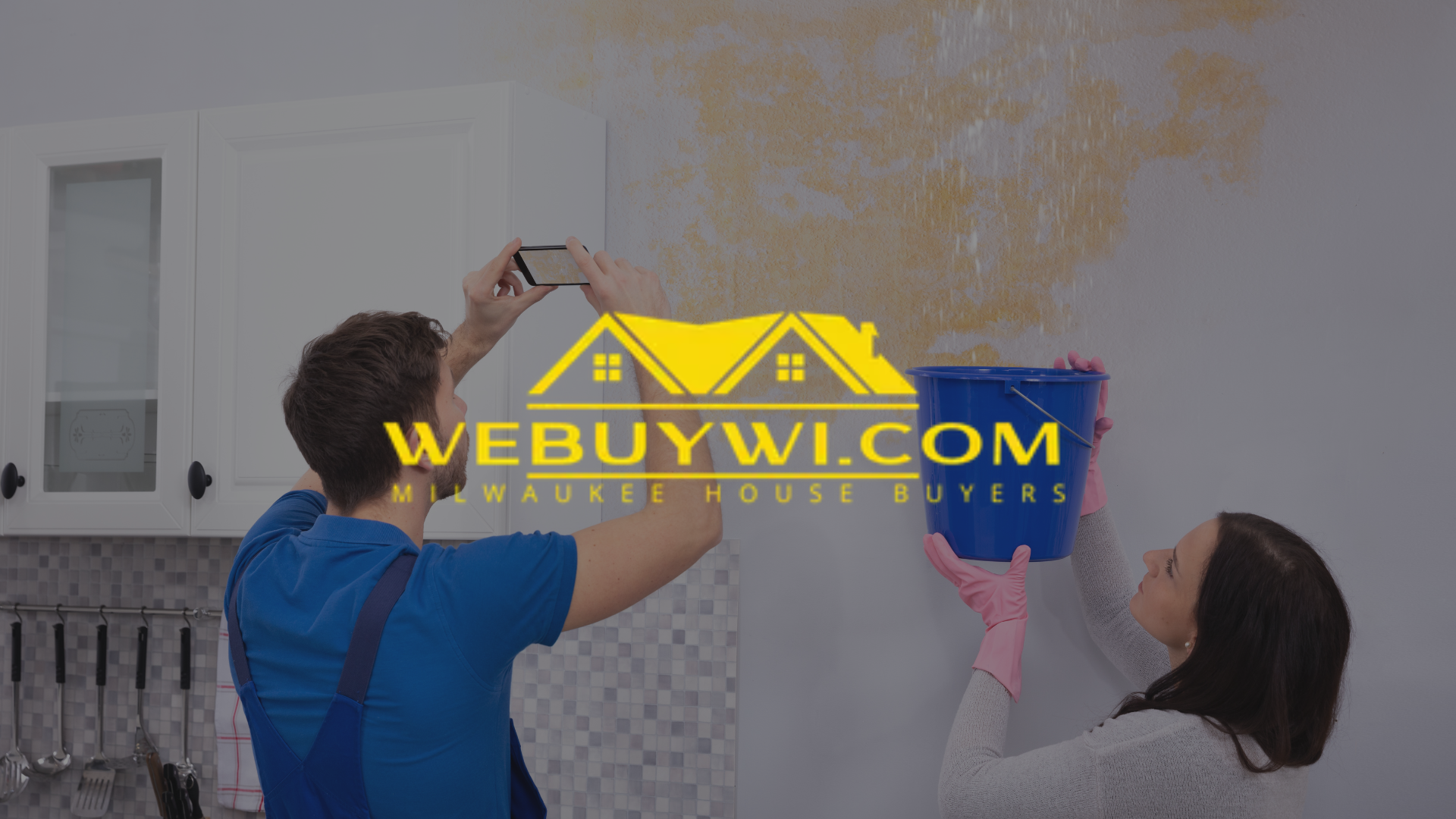 Two people taking photos of water damage on a wall, holding a bucket. The logo 