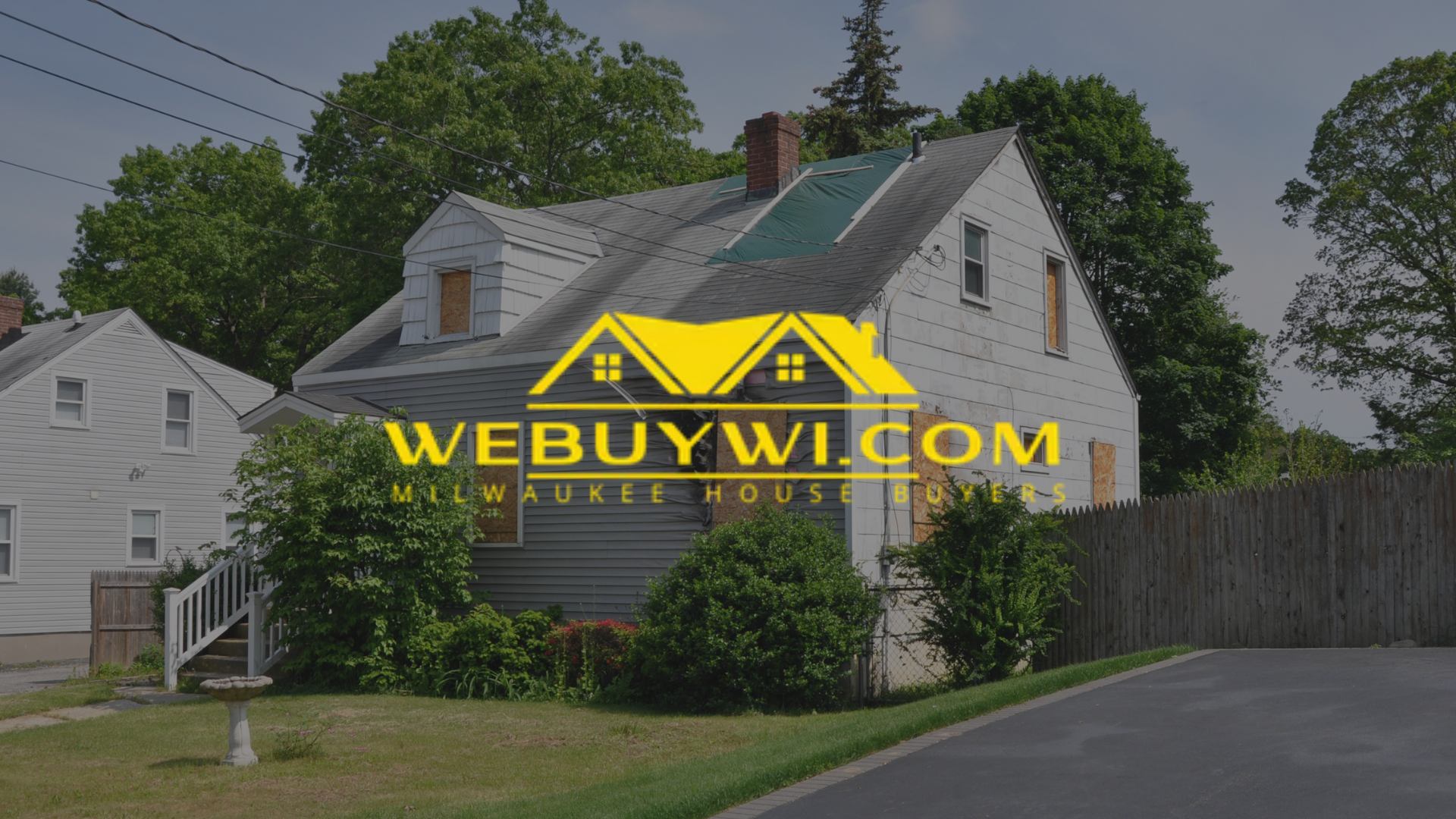 House with a WeBuyWI.com logo overlay. Grey house with green and yellow accents, street in front.