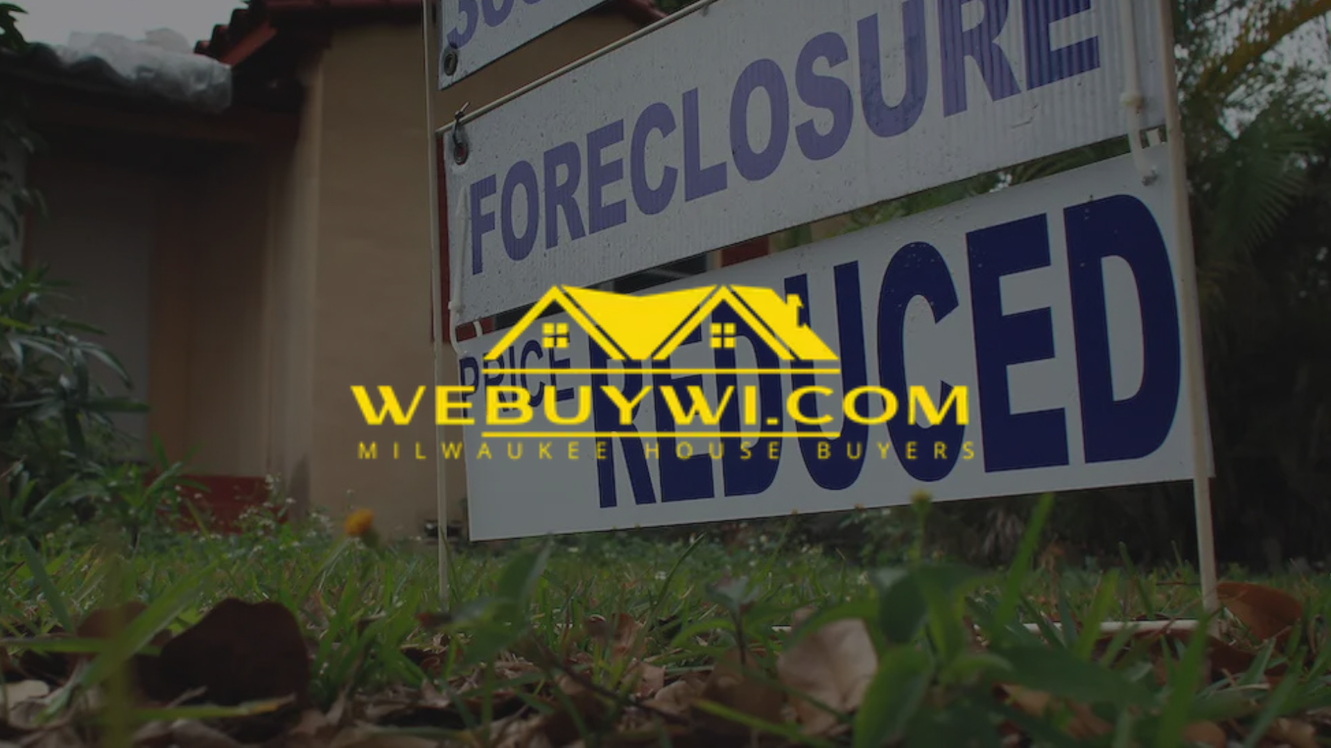 A foreclosure sign is sitting in the grass next to a building with webuywi.com logo on top