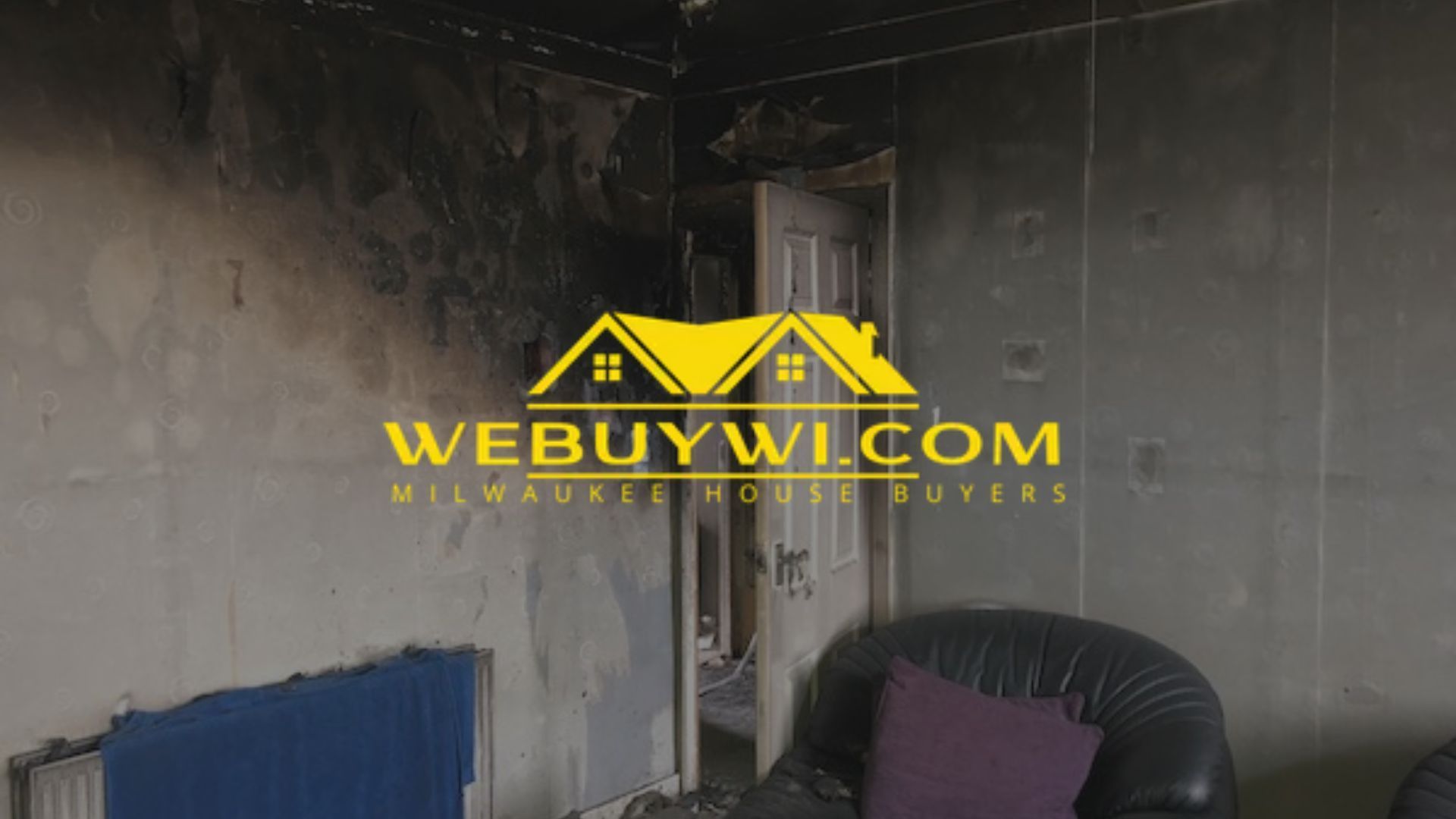 Interior of a room damaged by fire; walls and ceiling are blackened. Includes a door and a chair.
