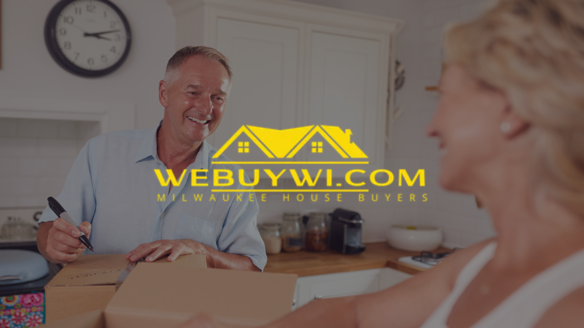 Man signing papers with woman, logo for WeBuyWI.com in kitchen.
