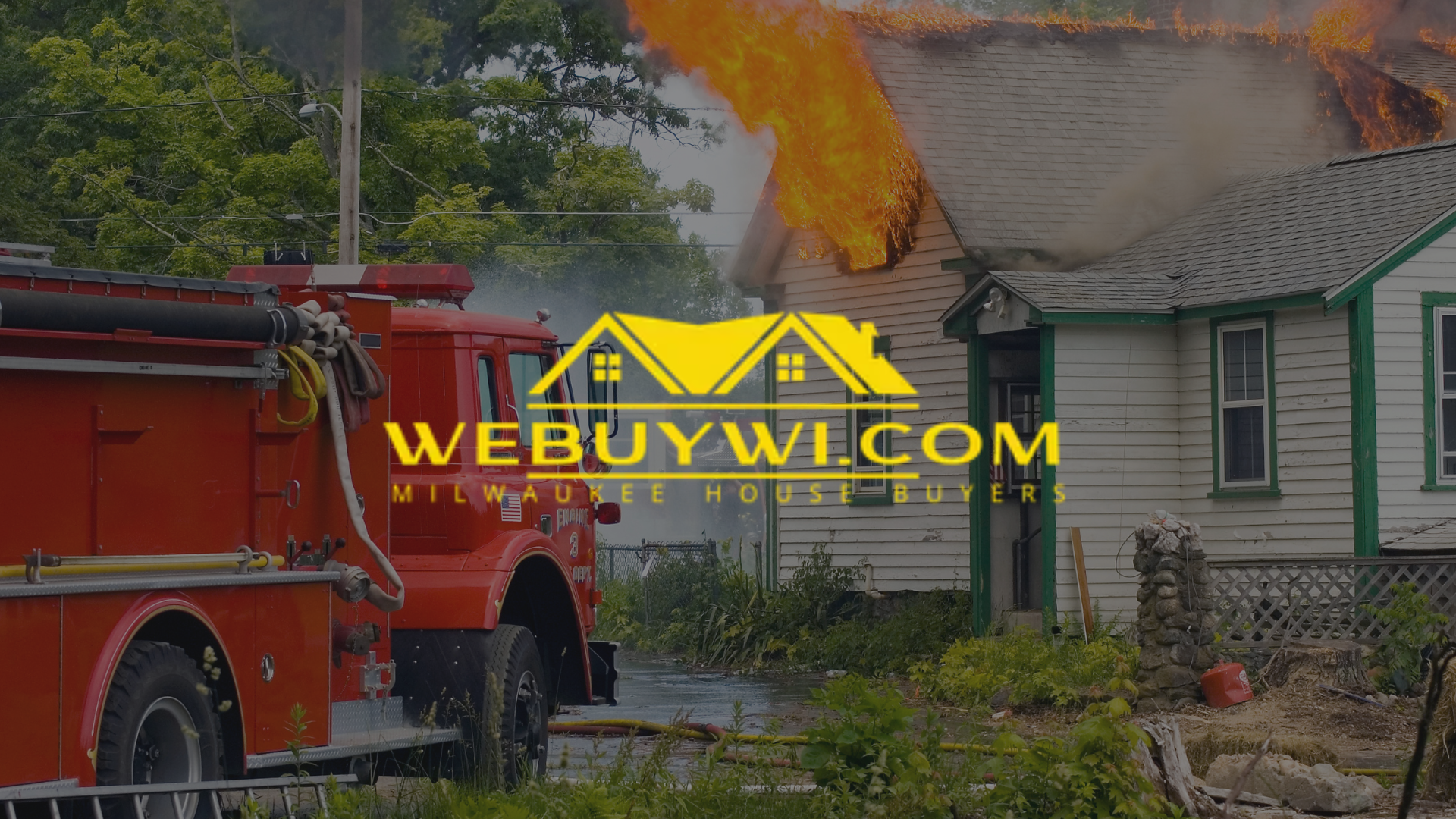 Fire engulfs a small house as a red fire truck stands nearby, spraying water.