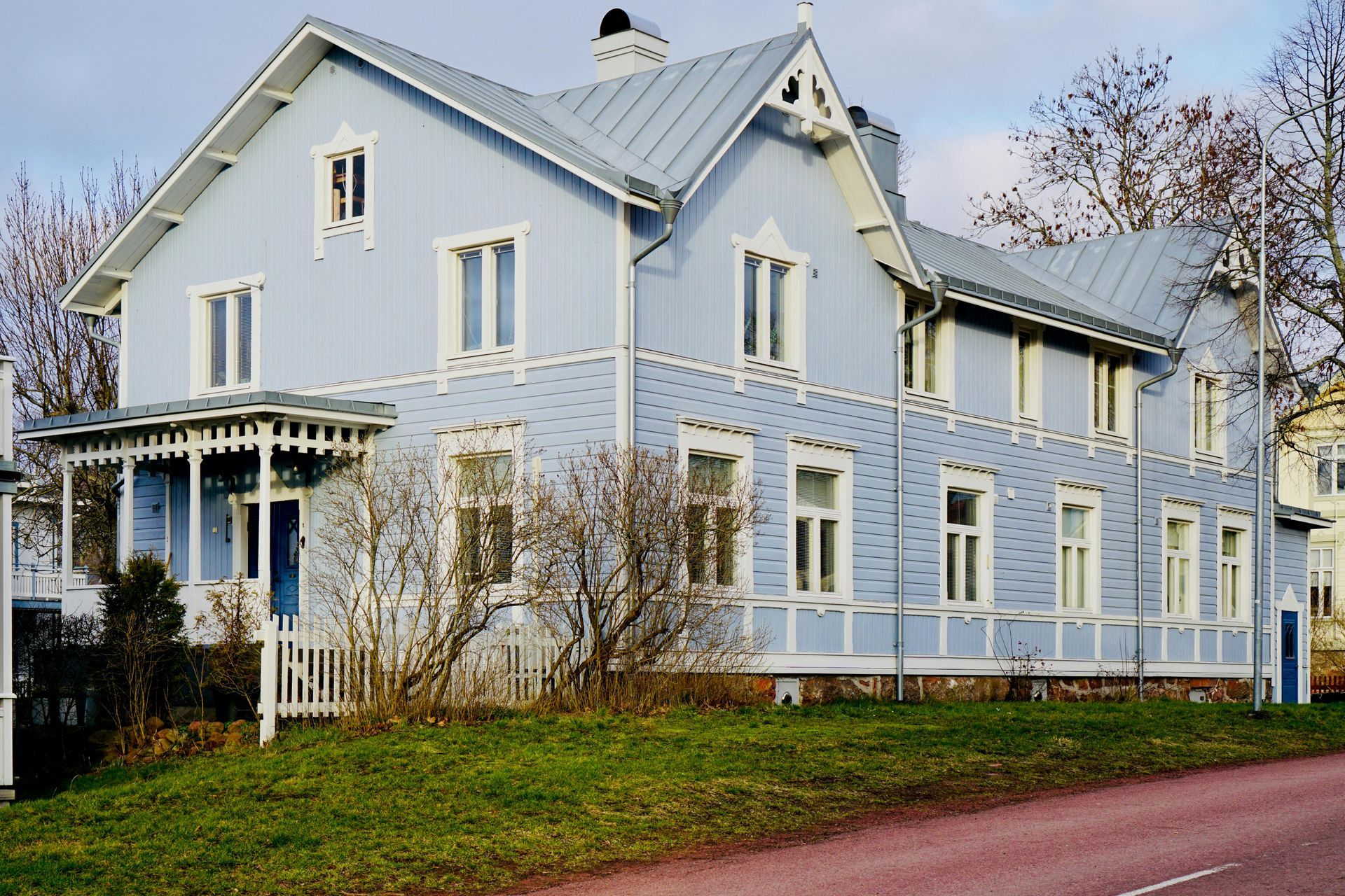 Light blue two-story wooden house with white trim, porch, and a light blue roof against a cloudy sky.