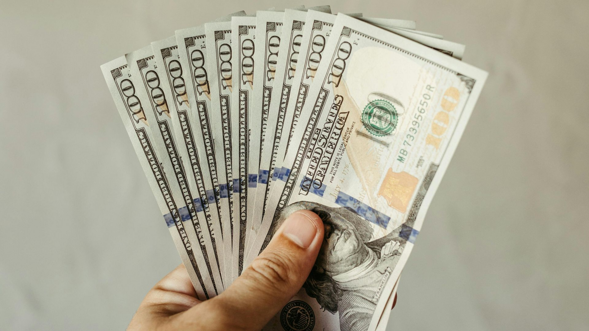 Hand holding a fan of US dollar bills against a plain background