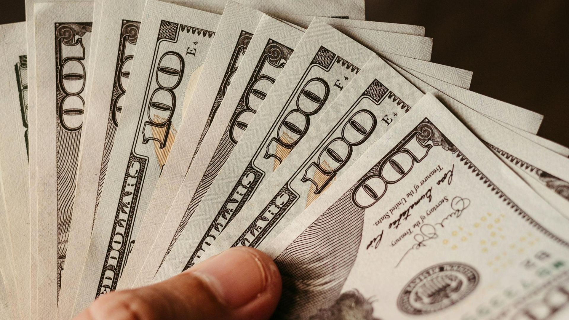 A hand fanned out several American one-hundred-dollar bills.