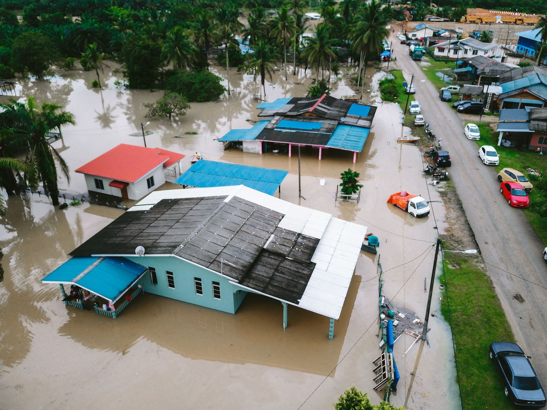 Flooded neighborhood with submerged houses, parked cars, and muddy water covering streets