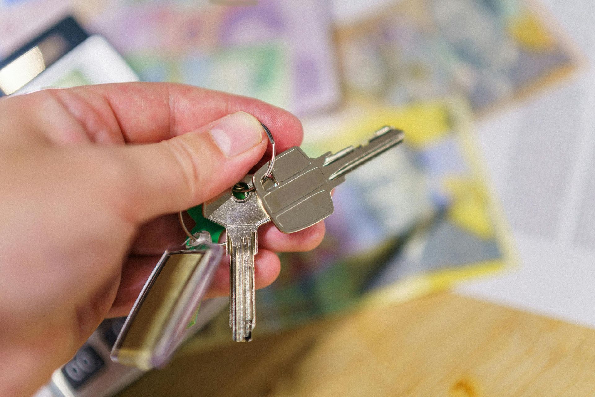 Hand holding a set of silver keys with money in the blurred background.