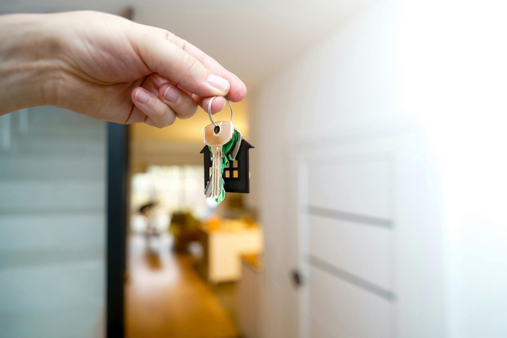 Hand holding keys with house-shaped keychain in front of an open doorway.