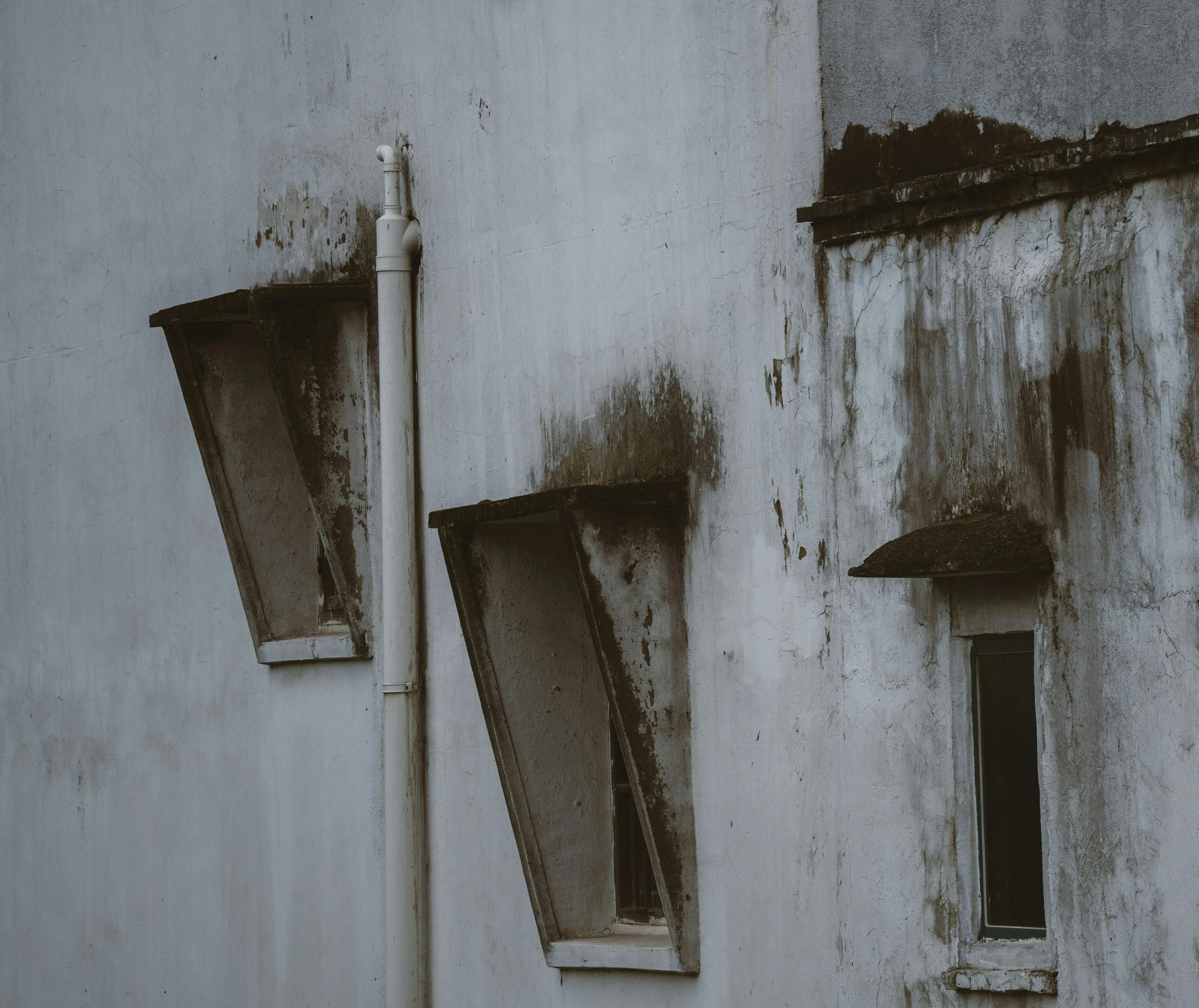 Weathered white wall with three small, grimy windows and dark stains around them
