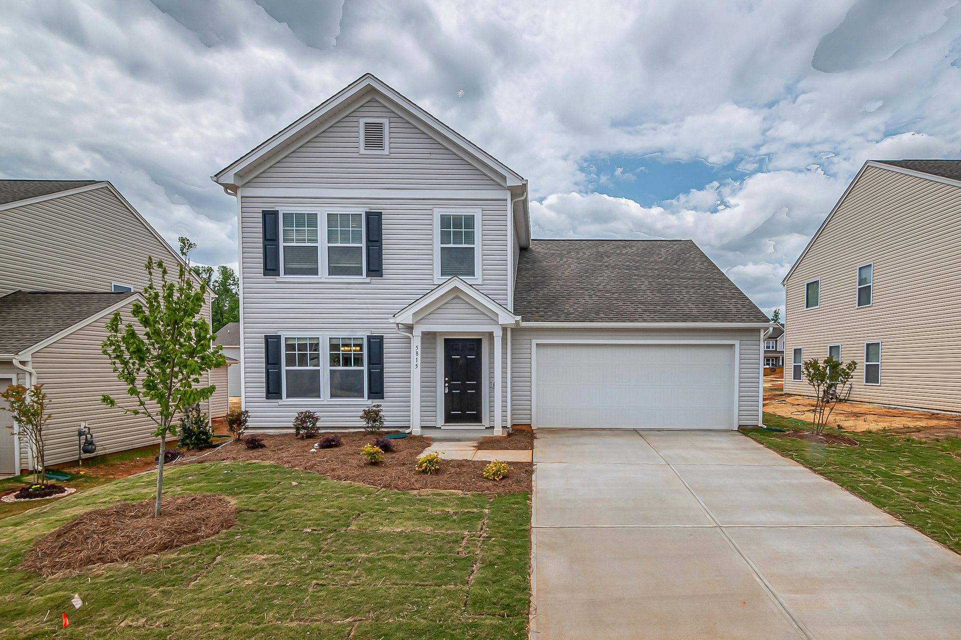 Light gray two-story house with black shutters, attached garage, and driveway on a cloudy day.