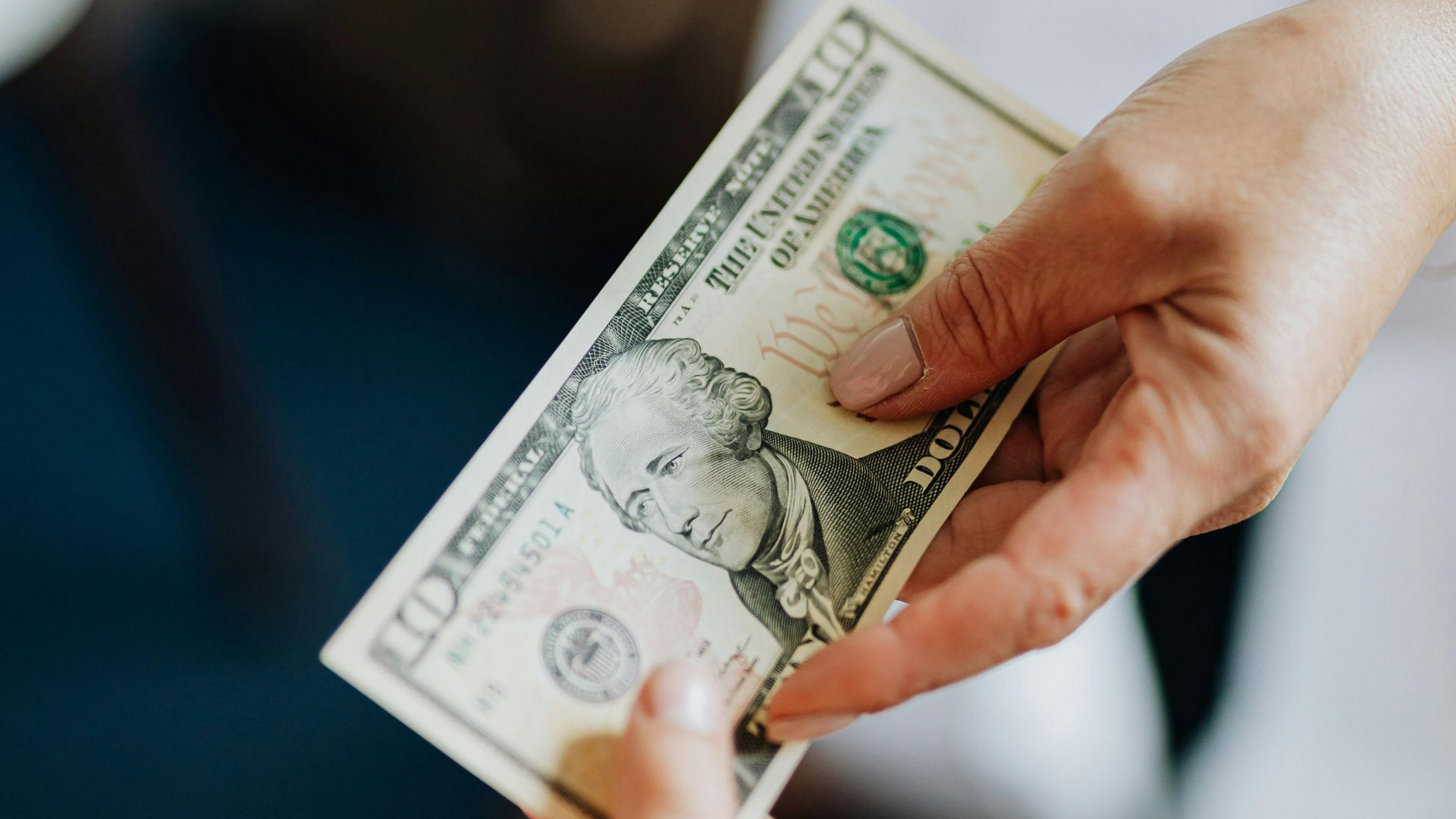 Hand holding a $100 bill in an indoor setting