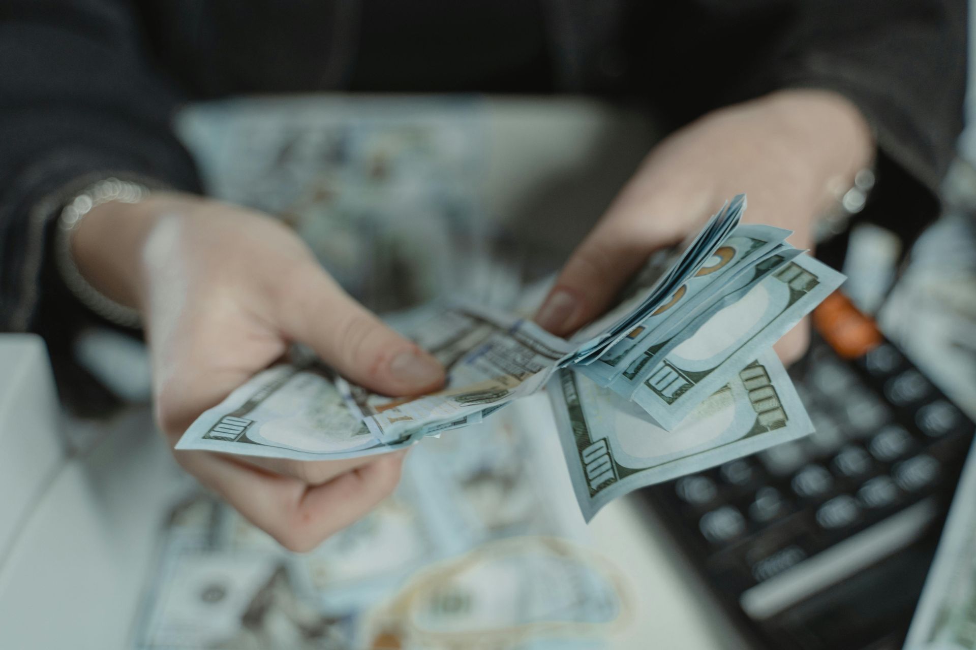Hands counting U.S. dollar bills over a keyboard, with scattered cash in the background