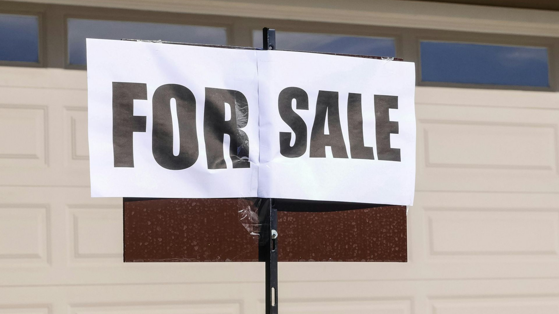 Hand exchanging house keys beside a red “HOME FOR SALE” sign