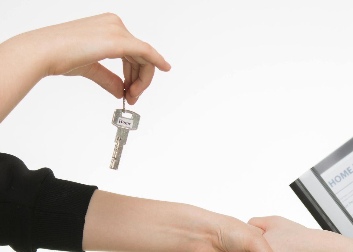 Two people shake hands while one holds a key and the other holds a home insurance policy folder.