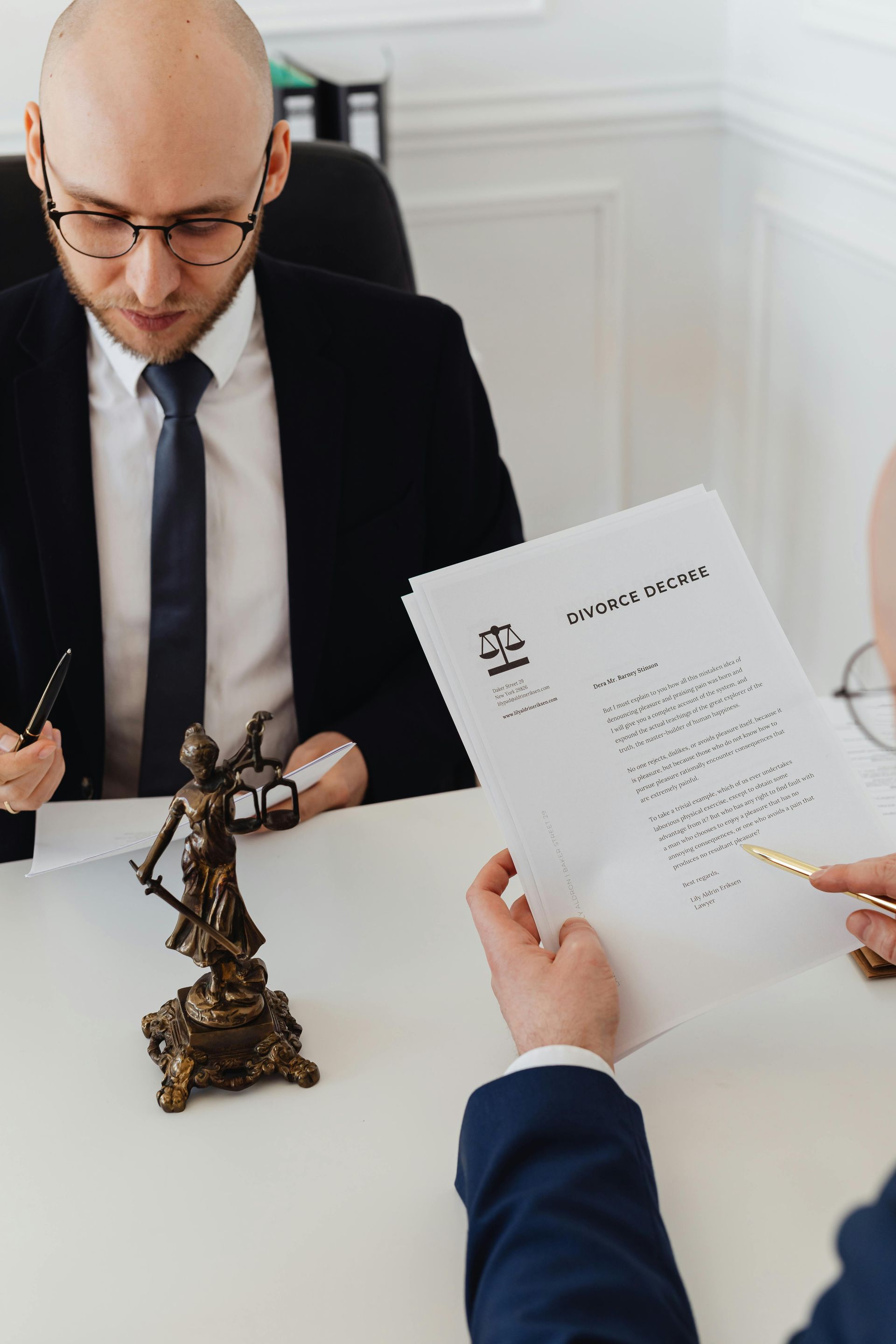 Businessman signing documents across a desk in a bright office, with a small statue in the foreground