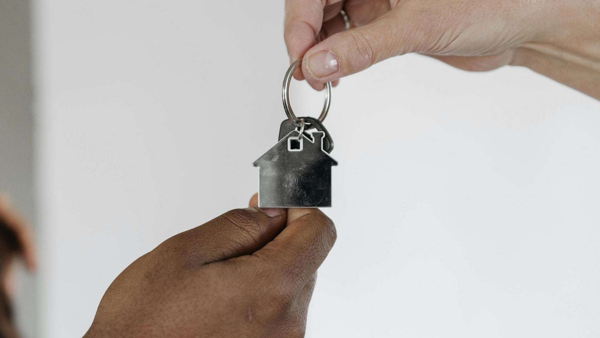Two people exchanging a house-shaped keychain, symbolizing a real estate transaction or new home.