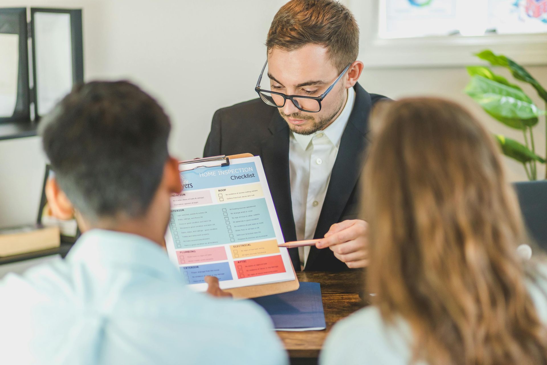 Man in suit points to a document for a couple, discussing financial information. Office setting.