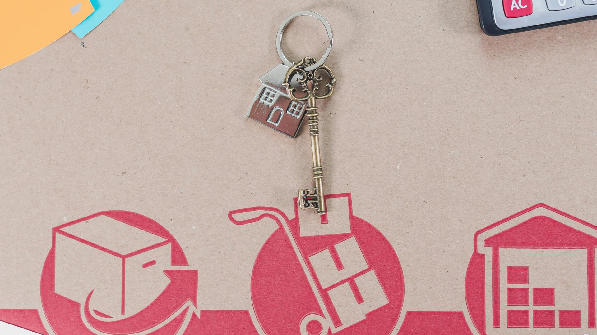 Key with house charm and moving icons on a cardboard box, suggesting relocation and new home.