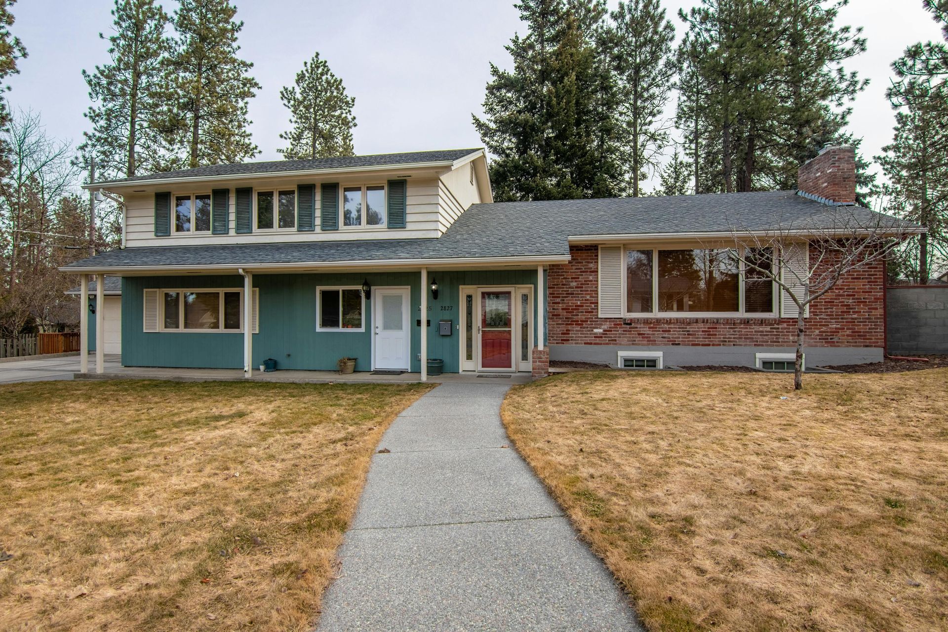 Two-story house with green and brick siding. A walkway leads to a red door.