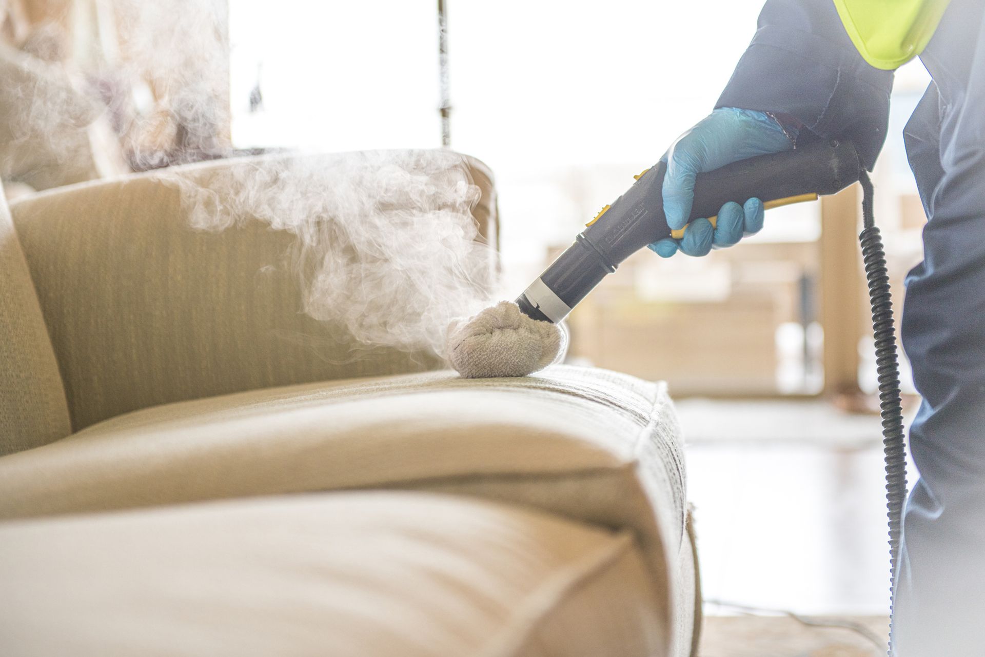 A person is cleaning a couch with a steam cleaner.