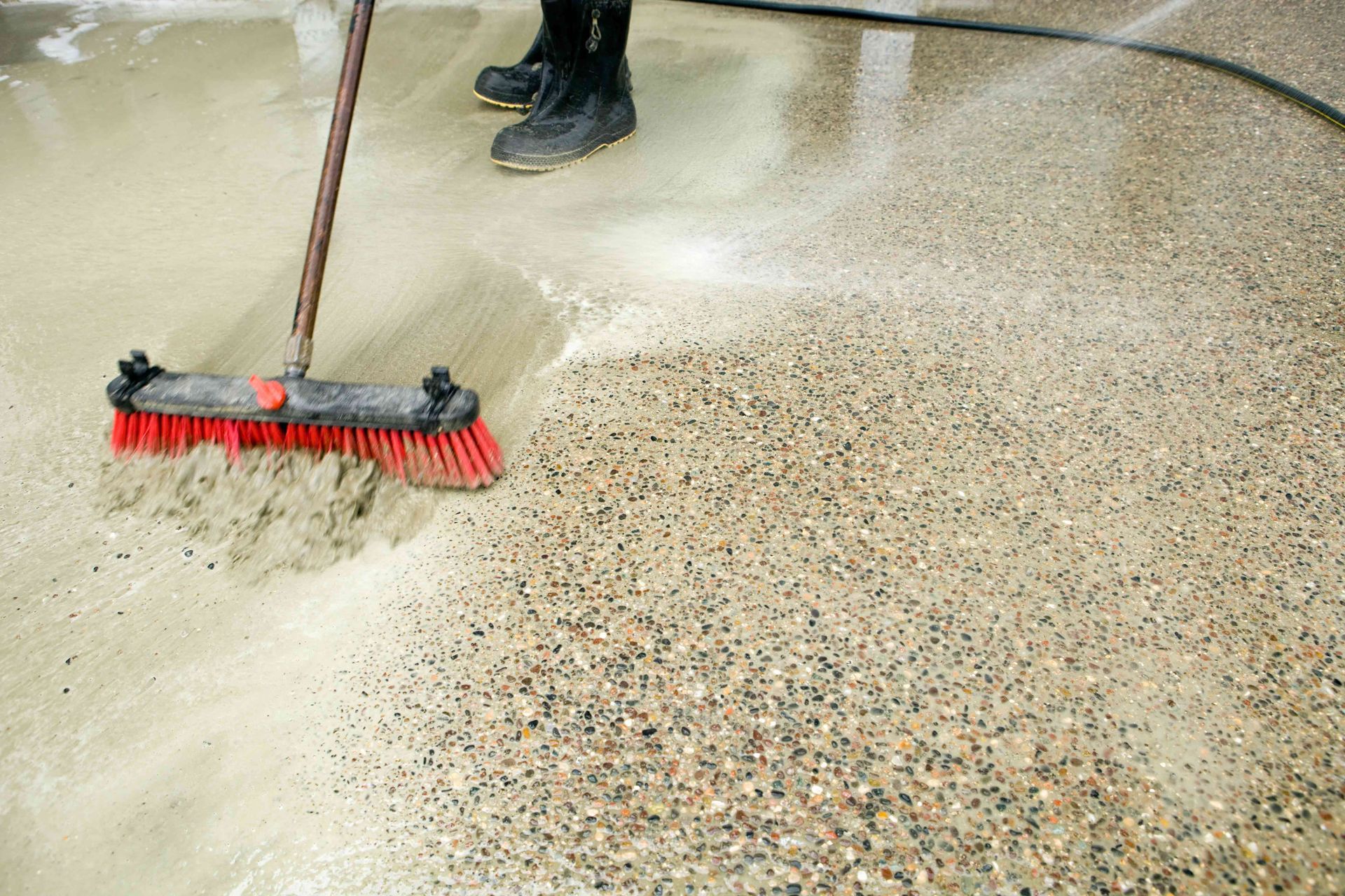 A person is cleaning a concrete floor with a broom.