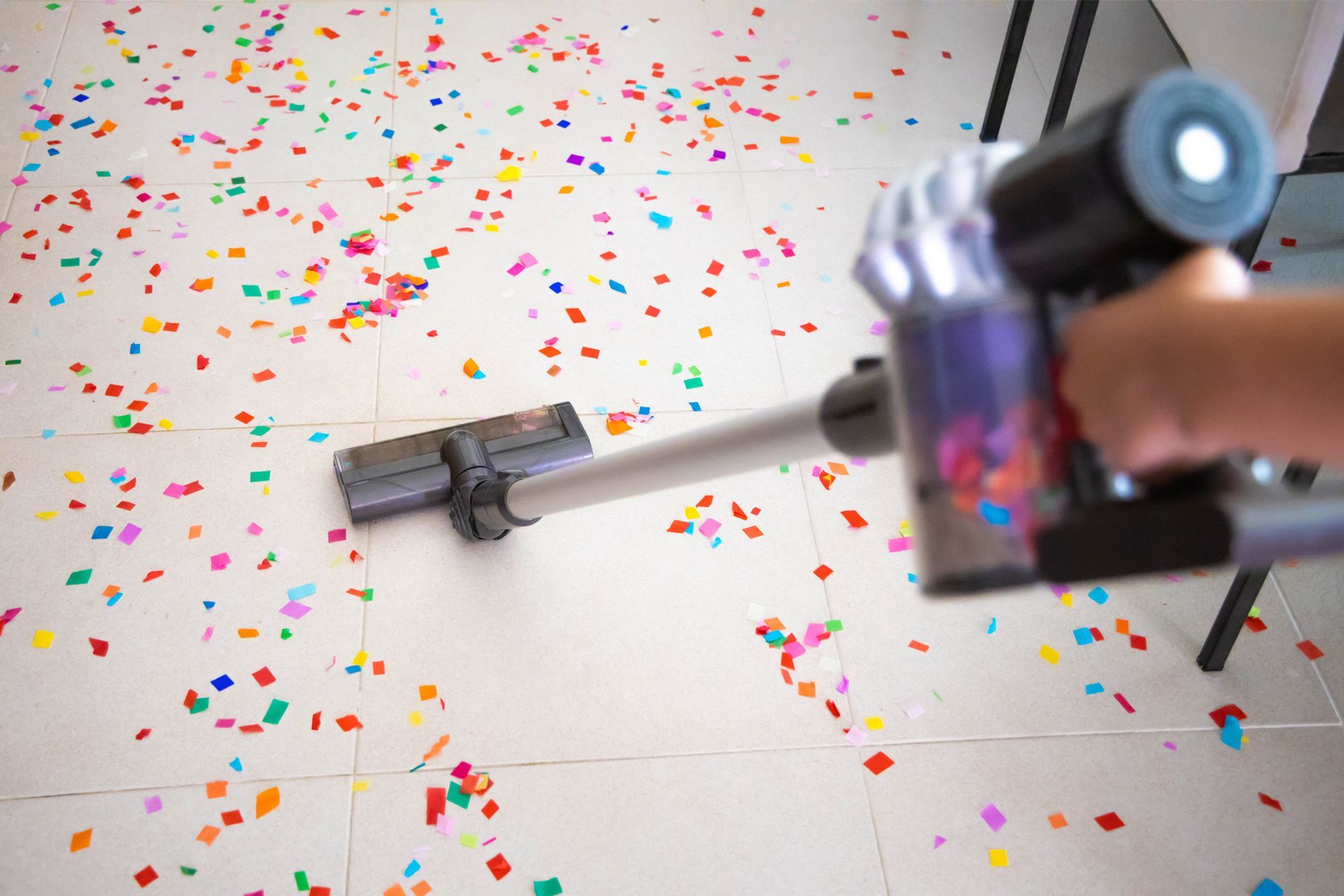 A person is using a vacuum cleaner to clean a floor covered in confetti.