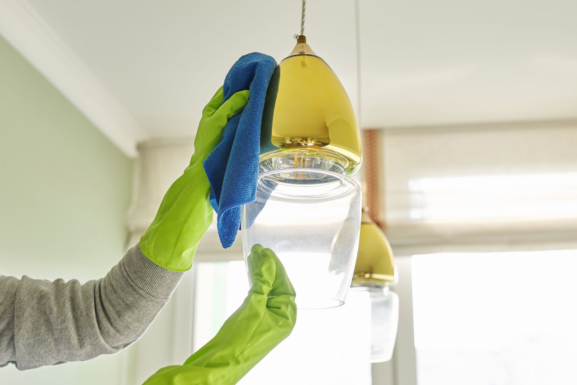 A person wearing green gloves is cleaning a light fixture with a cloth.