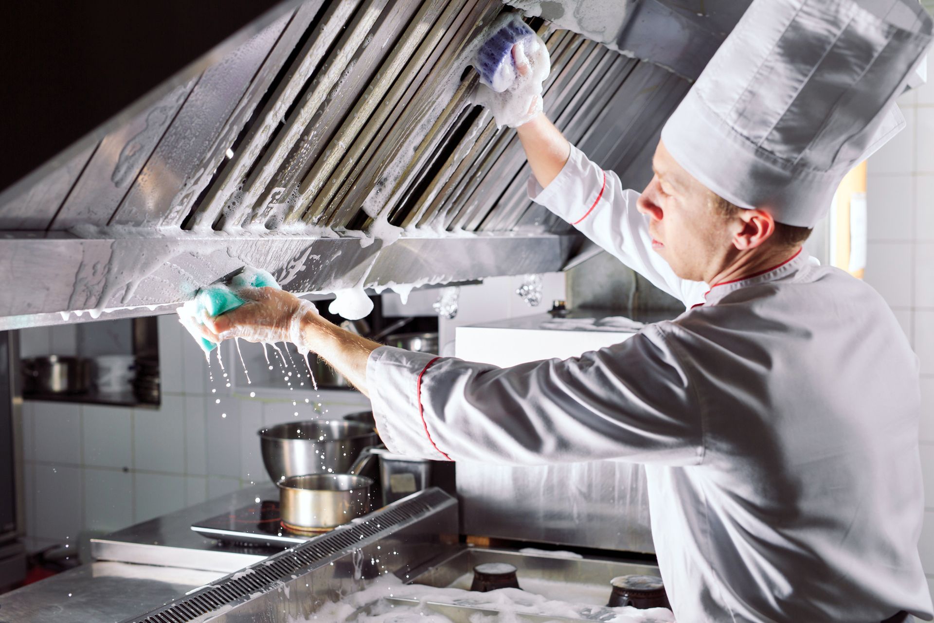 A chef is cleaning a hood in a kitchen with a sponge.